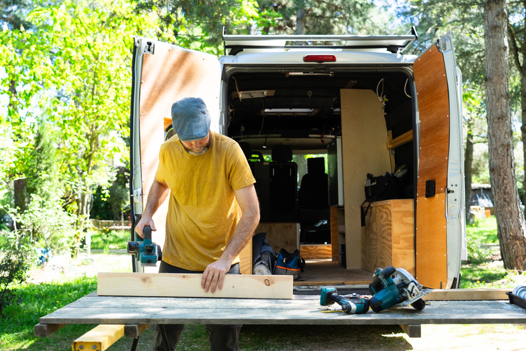 Carpenter working on wood plank, building camper van in nature