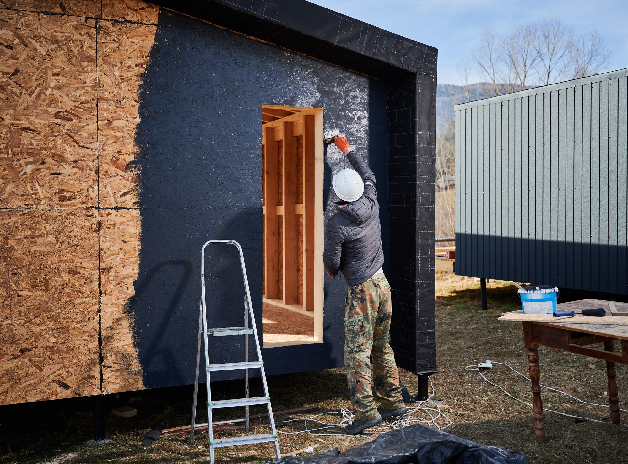 Male painter using paint roller, doing exterior paint work while building wooden frame house.